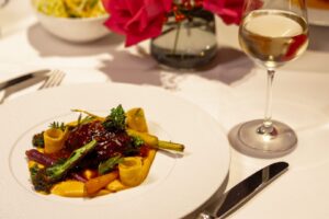 Geschmorte Kalbsbacke, Karotte in Texturen, Senfsaat Jus auf Teller im Restaurant mit Weinglas.